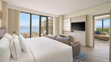 A hotel room with a large bed, a TV, a sofa, and a balcony with a view of the sea.