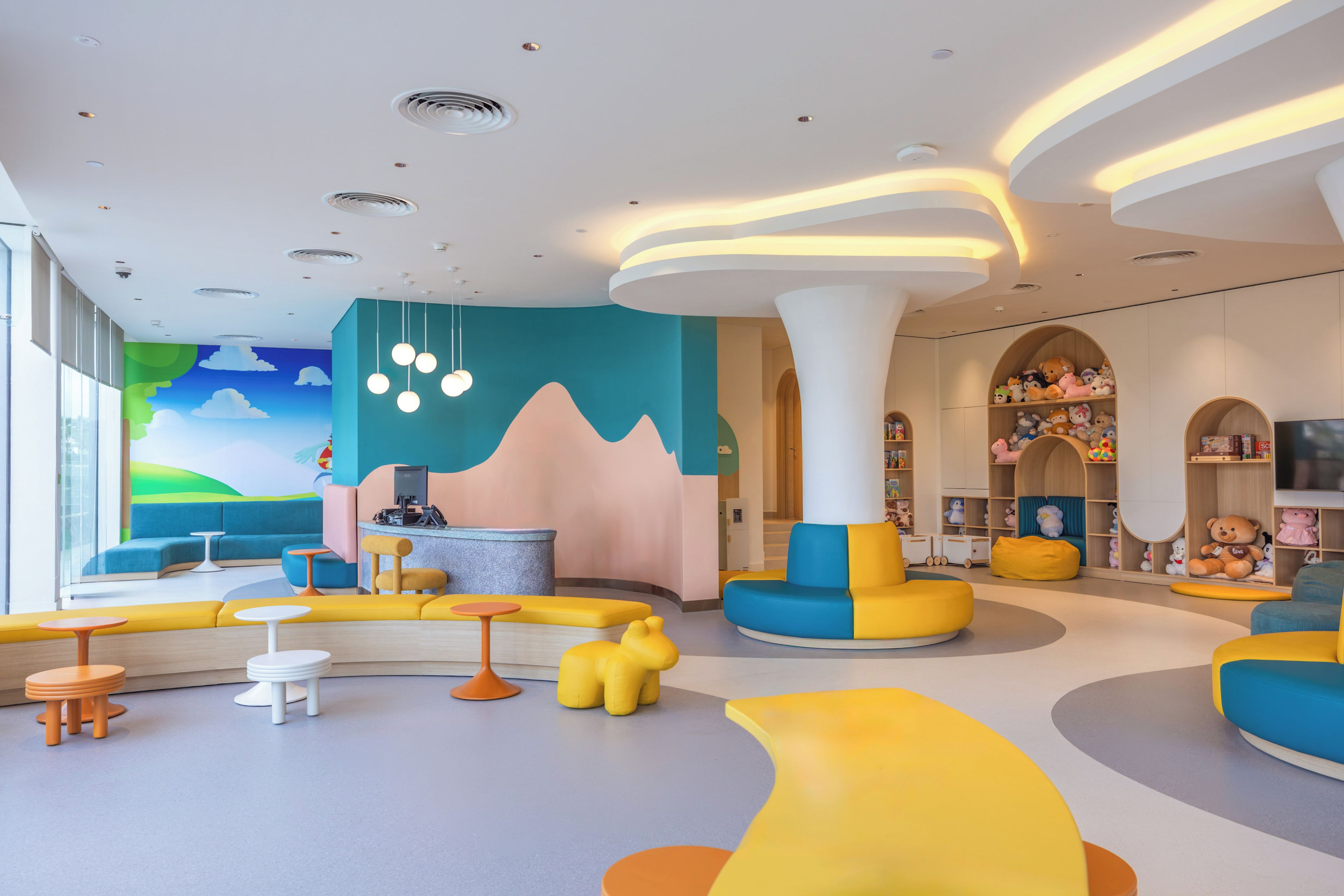 Un espace de jeux pour enfants aux couleurs vives, doté de sièges confortables et orné d’une fresque murale.