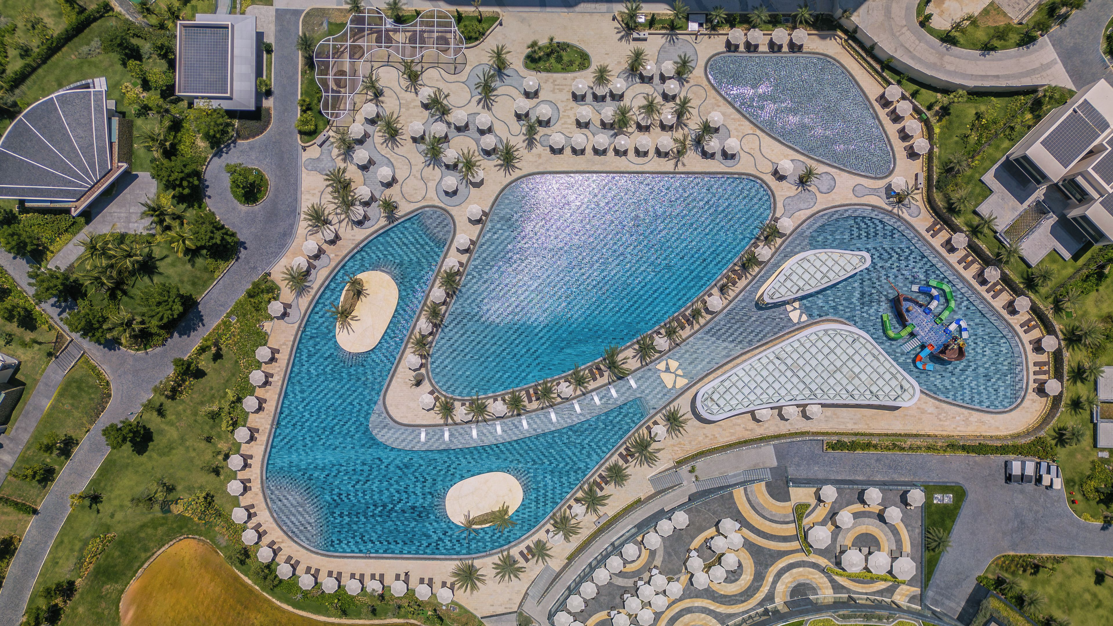 An aerial view of a resort with multiple swimming pools, sun loungers, and palm trees.