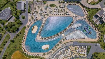 An aerial view of a resort with multiple swimming pools, sun loungers, and palm trees.