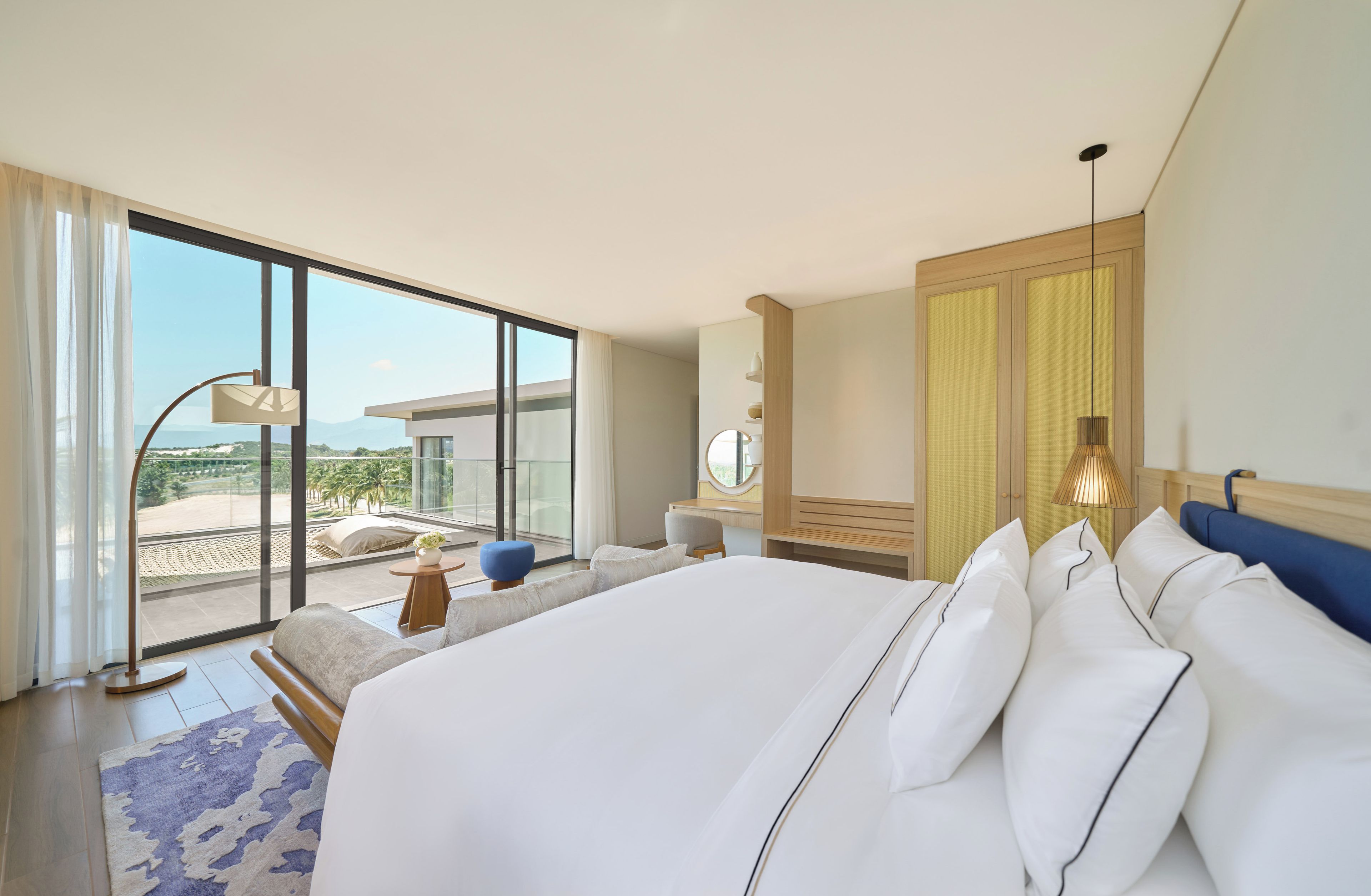 A modern hotel room with a large bed, a seating area, a view of the beach, and a balcony.