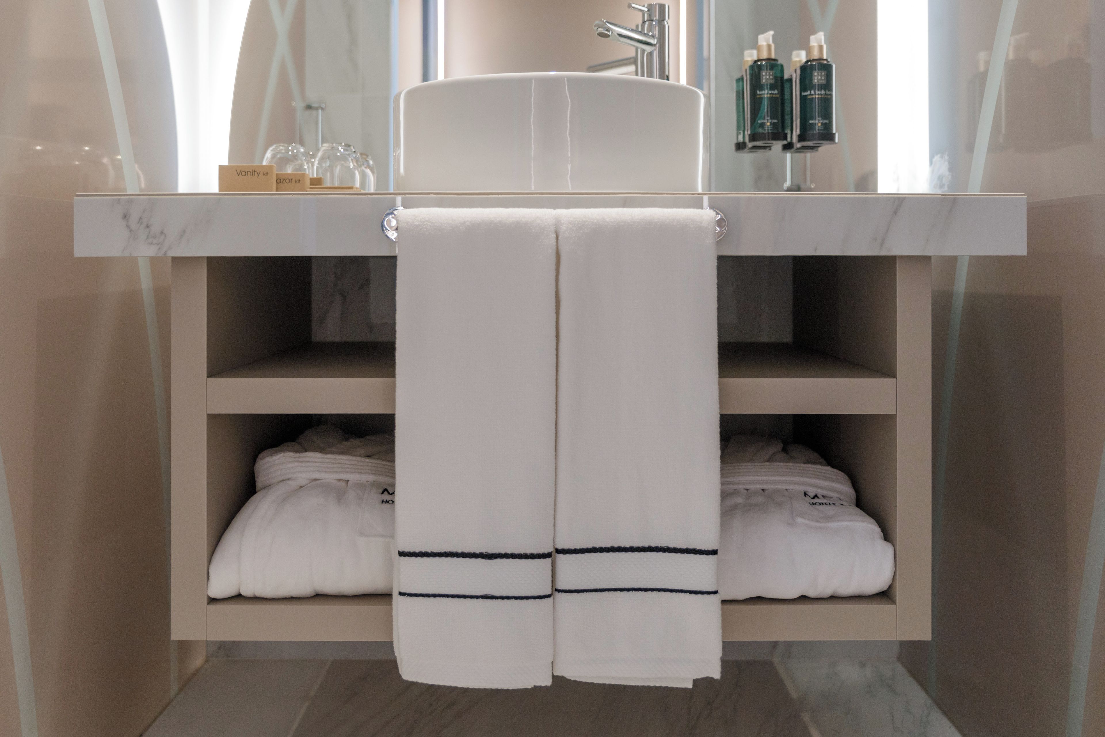 A bathroom with a marble sink, two shelves with folded towels, and a mirror above the sink.