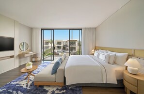 A modern hotel room with a large bed, a TV, a desk, and a view of a pool and buildings. - Melia Serenity Cam Ranh Beach Resort (Cam Lam)