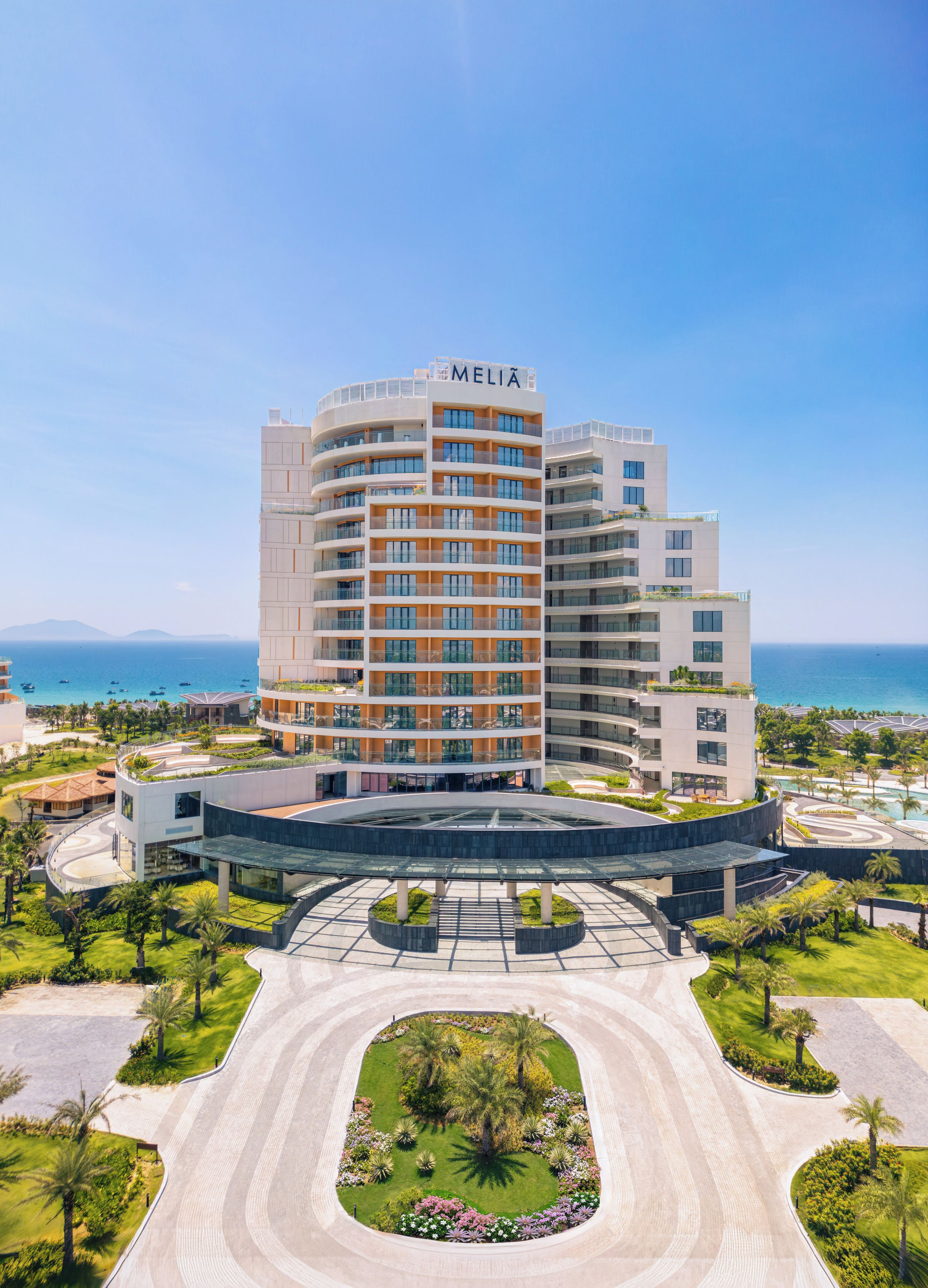 Un hotel de varios pisos con un patio central, rodeado de vegetación y vistas al mar.