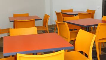 A room with orange tables and chairs, a world map on the wall, and two small paintings.