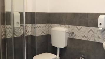 A bathroom with a glass shower enclosure, a toilet, and a bidet.