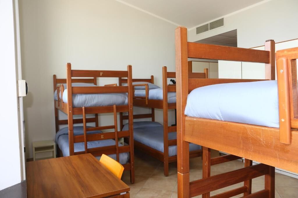 Una habitación con literas, una mesa de madera y un taburete pequeño.