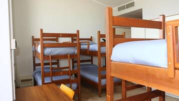 Una habitación con literas, una mesa de madera y un taburete pequeño.
