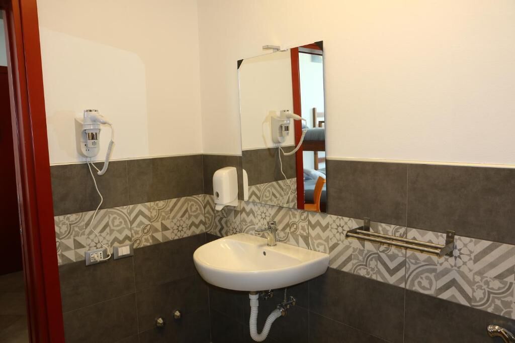 Une salle de bain avec un lavabo blanc, un miroir, un porte-serviettes et des carreaux à motifs.