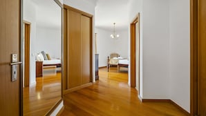 A hallway with wooden flooring leading to two bedrooms, each with a bed and a nightstand. - Villa Lucente by Homie (Funchal)