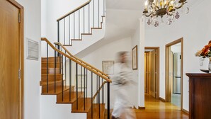 A staircase with wooden steps and black railings, leading to a room with a chandelier and framed pictures on the walls. - Villa Lucente by Homie (Funchal)