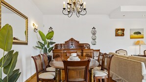 A dining area with a round wooden table, six chairs, a chandelier, and wall-mounted decor. - Villa Lucente by Homie (Funchal)