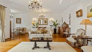 A spacious living room with a large chandelier, a sofa set, a dining table, and a coffee table. - Villa Lucente by Homie (Funchal)
