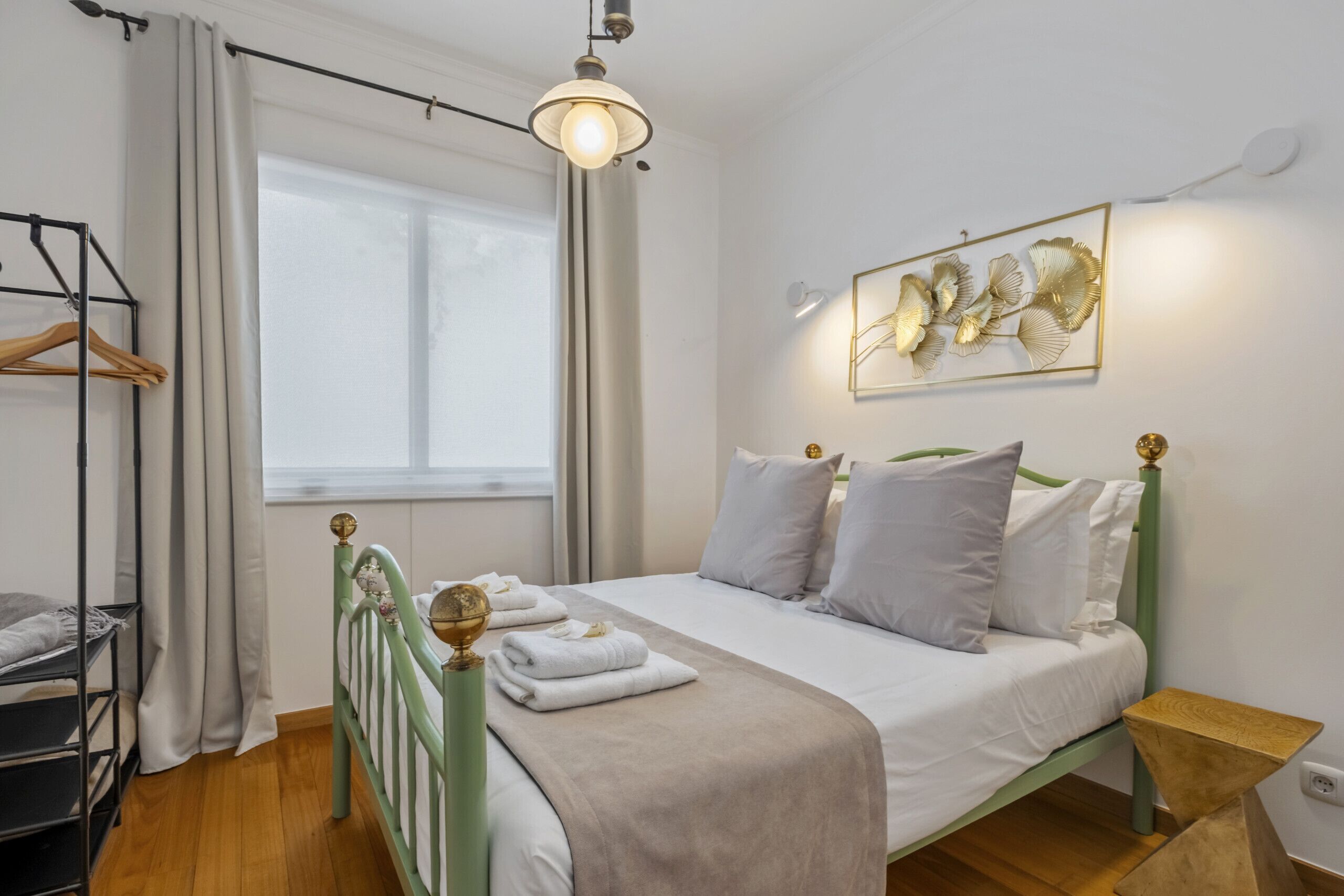 A neatly arranged bedroom with a bed, a bedside table, a hanging light fixture, and a window with curtains.