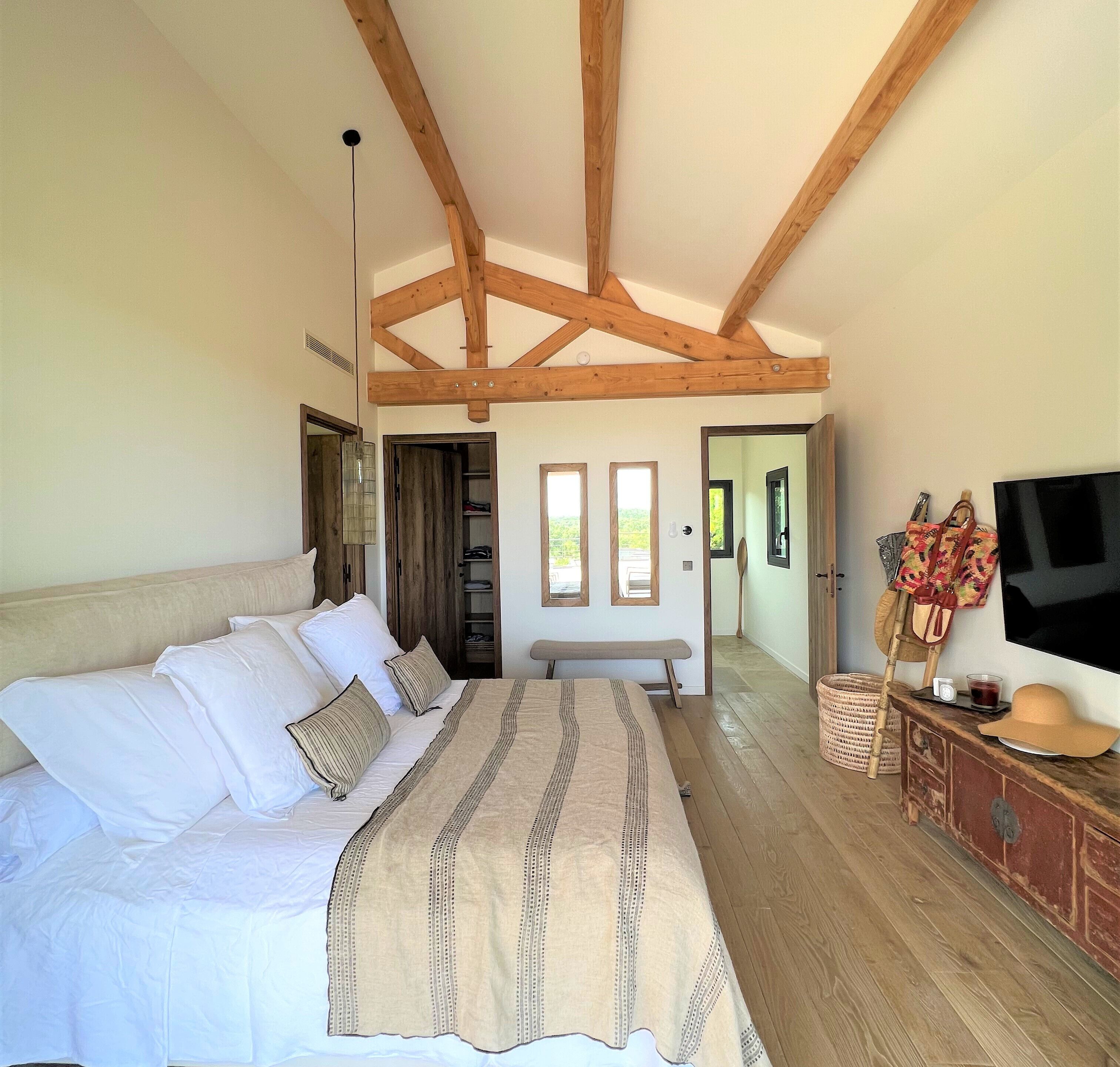 Ein Schlafzimmer mit einem großen Bett, Holzbalken, einem Fernseher und einem Kleiderschrank.