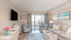 Una sala de estar con un sofá, dos sillones, una mesa de centro, un televisor y un cuadro.