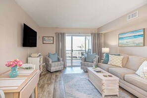 A living room with a sofa, two armchairs, a coffee table, a TV, and a painting. - Waterfront Condo with Pool & Boat Slip (Ocean City)
