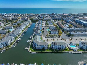 An aerial view of a marina with multiple buildings, boats, and a clear view of the ocean. - Waterfront Condo with Pool & Boat Slip (Ocean City)