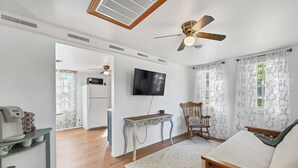 A living room with a wooden floor, a ceiling fan, a TV, a wooden chair, a coffee machine, and a table. - Cozy 1-bedroom cottage with waterfront views (Townsend)