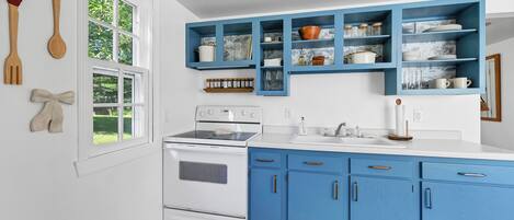 Una cocina con armarios blancos y azules, una estufa y una ventana con vistas a la vegetación.