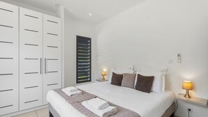 Ein Schlafzimmer mit Bett, Nachttischlampen, einem Kleiderschrank und einem Fenster mit Jalousien.
