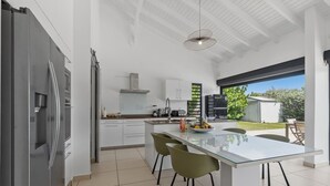 Eine moderne Küche mit einer zentralen Kochinsel, weißen Schränken und Blick ins Freie.