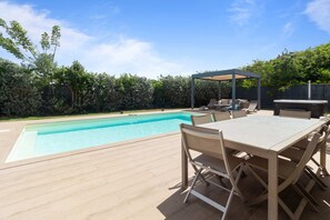 A swimming pool with a wooden deck, outdoor seating, and a covered area.