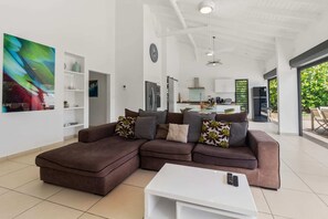 A modern living room with a sectional sofa, a white coffee table, and a kitchen in the background.