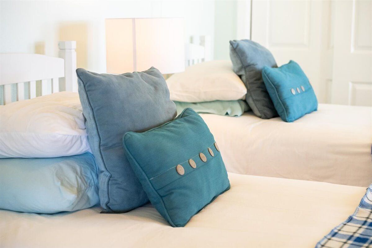 A bed with multiple pillows in various colors, a white headboard, and a bedside table with a lamp.