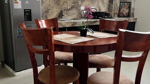 Un coin repas comprenant une table ronde en bois, quatre chaises, un réfrigérateur, un pare-feu en marbre et un évier.
