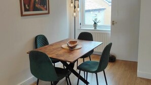 Un comedor con una mesa de madera y cuatro sillas, un cuadro en la pared y una ventana con vistas a edificios.
