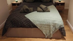 Un dormitorio con una cama, dos mesitas de noche, un ventanal y una lámpara de techo.