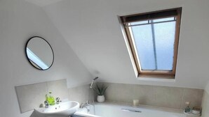 Un baño moderno con tragaluz, lavamanos pedestal, bañera y retrete.