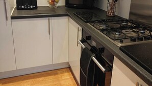 Una cocina moderna con armarios blancos, encimera negra, estufa a gas, tostadora, microondas y un frutero.