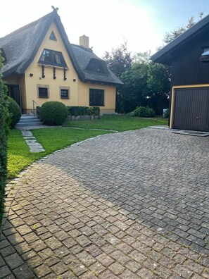 Ein Haus mit einem steilen Satteldach, einer Veranda und einer gepflasterten Auffahrt, die zu einer Garage führt.