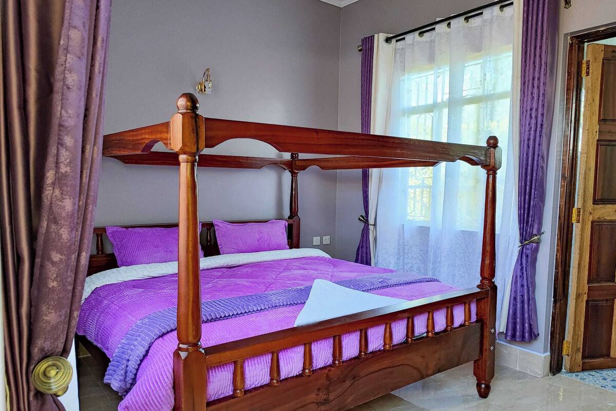 A four-poster bed with a wooden frame and purple bedding.