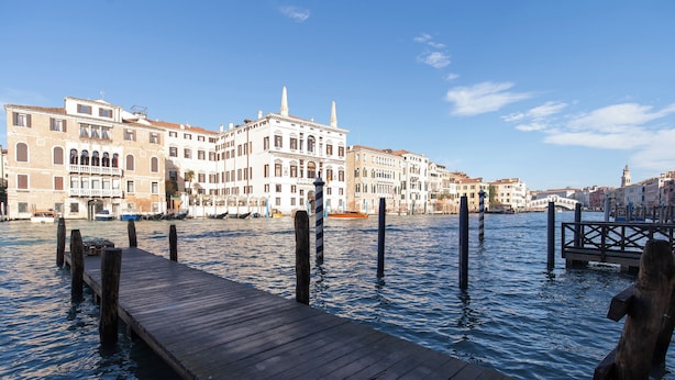 Un muelle de madera que se extiende sobre un canal, con edificios históricos al fondo.