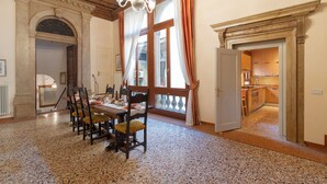 Un comedor con una mesa y sillas de madera, un candelabro y ventanas grandes con cortinas.