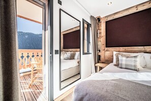 A bedroom with a wooden headboard, a large mirror, and a view of a balcony with a wooden deck and chairs. - Danton – Mountain View Apartment & Jacuzzi, Châtel (Châtel)