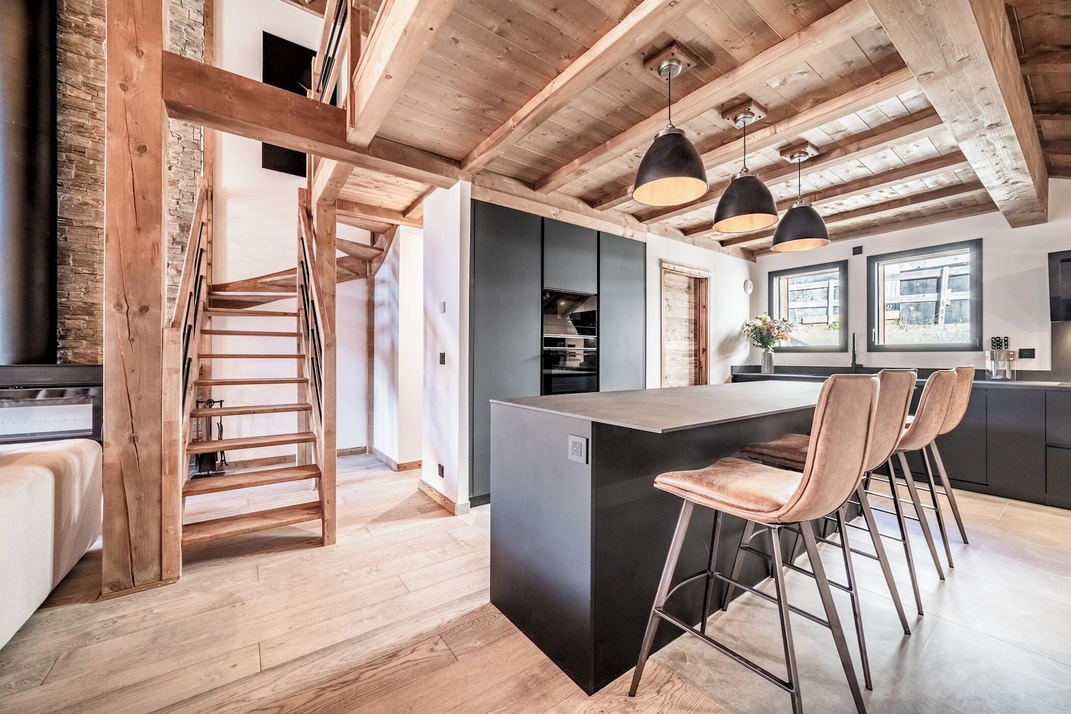 Een moderne keuken met een centraal kookeiland, barkrukken en hanglampen.