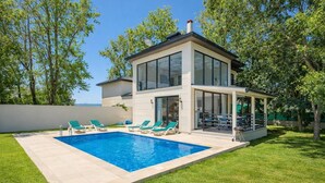 Ett modernt hus i två våningar med en swimmingpool, en grön gräsmatta och träd.