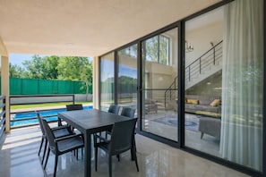 A modern outdoor patio with a dining table and chairs, a pool, and a view of the interior living area through large sliding glass doors. - Villa Ana - Three Bedroom Villa, Sleeps 6 (Merkez)