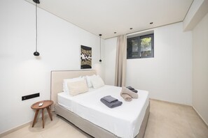 Ein modernes Schlafzimmer mit einem großen Bett, einem Nachttisch, einem Fenster mit Vorhängen und einem an der Wand befestigten Kunstwerk.