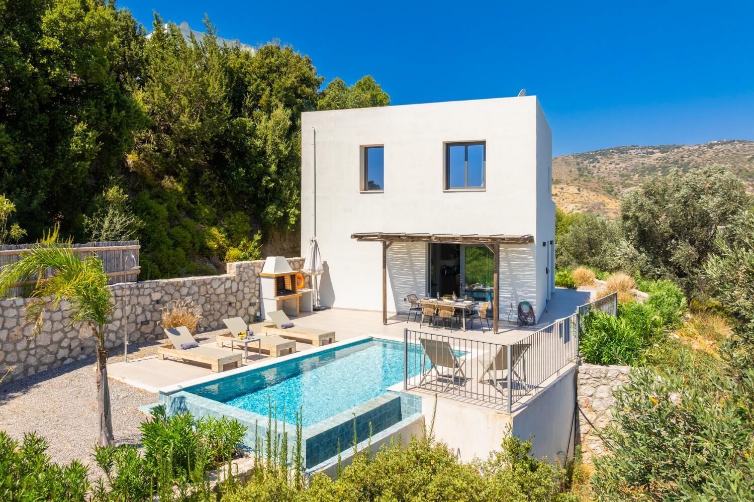 A modern two-story house with a swimming pool, outdoor seating, and a stone wall.