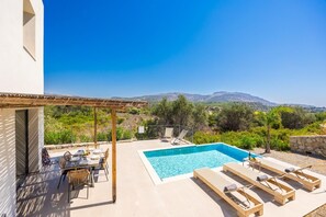 Ein Poolbereich mit Pergola, Liegestühlen und einem Esstisch, mit Blick auf eine Berglandschaft.