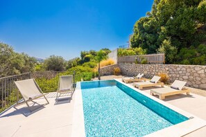 A pool with lounge chairs and a stone wall. - Massari Hills Moon Villa (Archangelos)