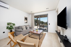 Una sala de estar moderna con un sofá gris, sillones de mimbre, una mesa de centro, un televisor de pantalla plana y un ventanal corredero que da a un espacio exterior.