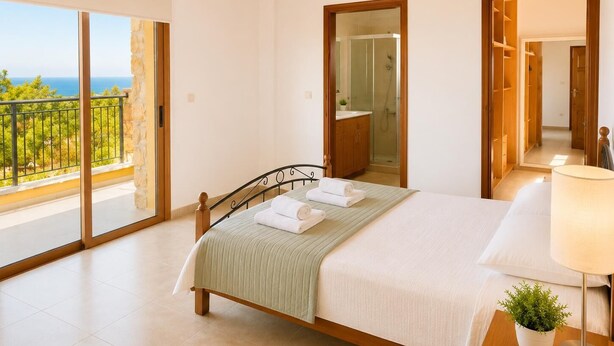 Een slaapkamer met een bed, een bedlamp, een potplant, een badkamer met douche en een balkon met uitzicht.