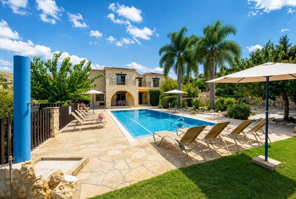 A swimming pool with lounge chairs, a stone building, and palm trees.