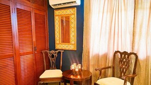 Una habitación con un armario de madera, una mesa con sillas, aire acondicionado instalado en la pared y una ventana con cortinas.